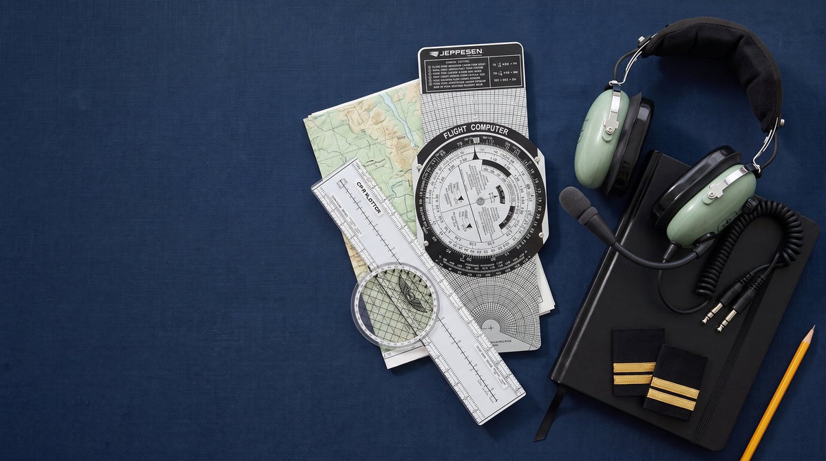 Equipo de estudiante de piloto sobre fondo azul marino: computador de vuelo Jeppesen E6B, plotter rotativo ASA, headset David Clark H10-13.4, bitácora, charreteras de una barra, carta de navegación y lápiz.
