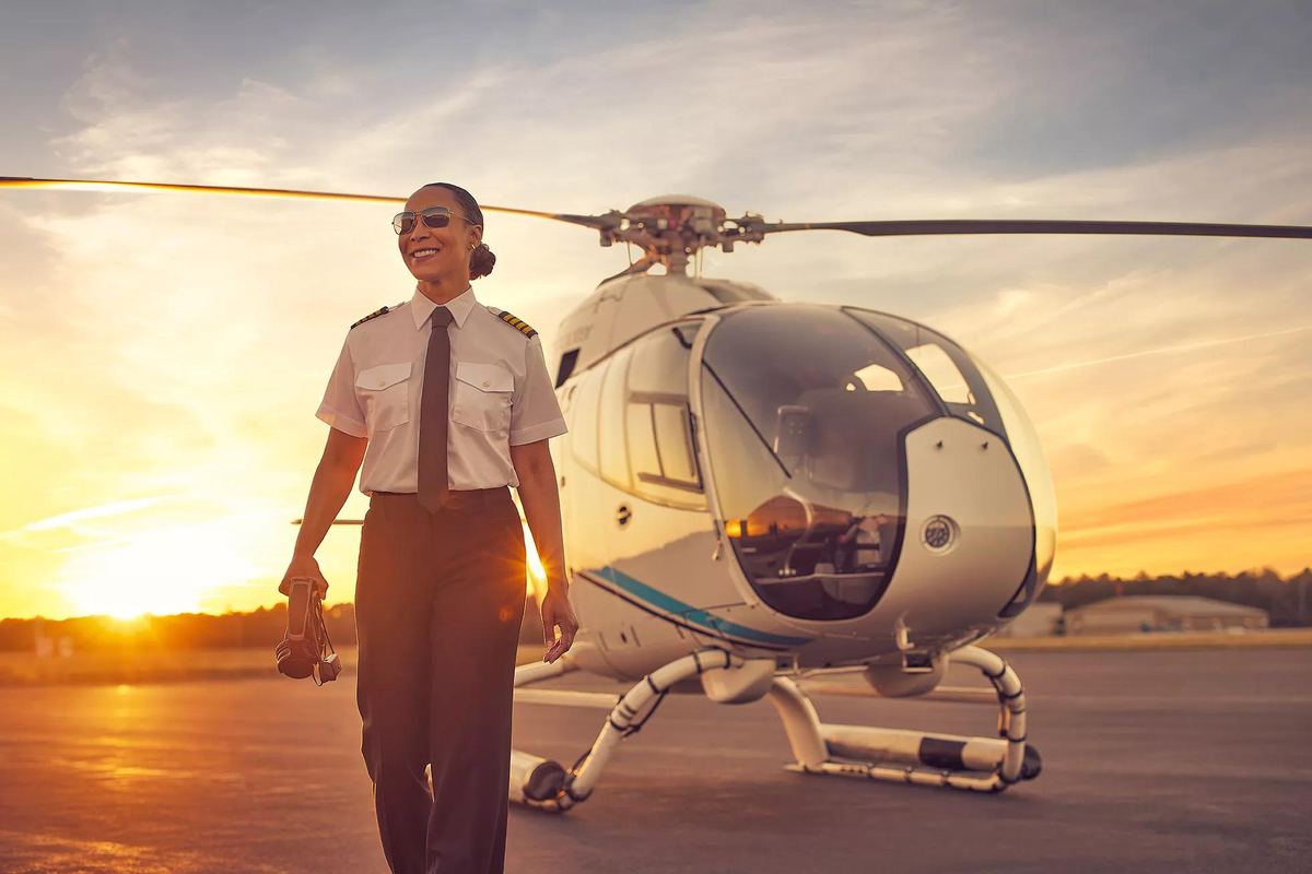 Piloto con camisa blanca y charreteras camina hacia un helicóptero al atardecer