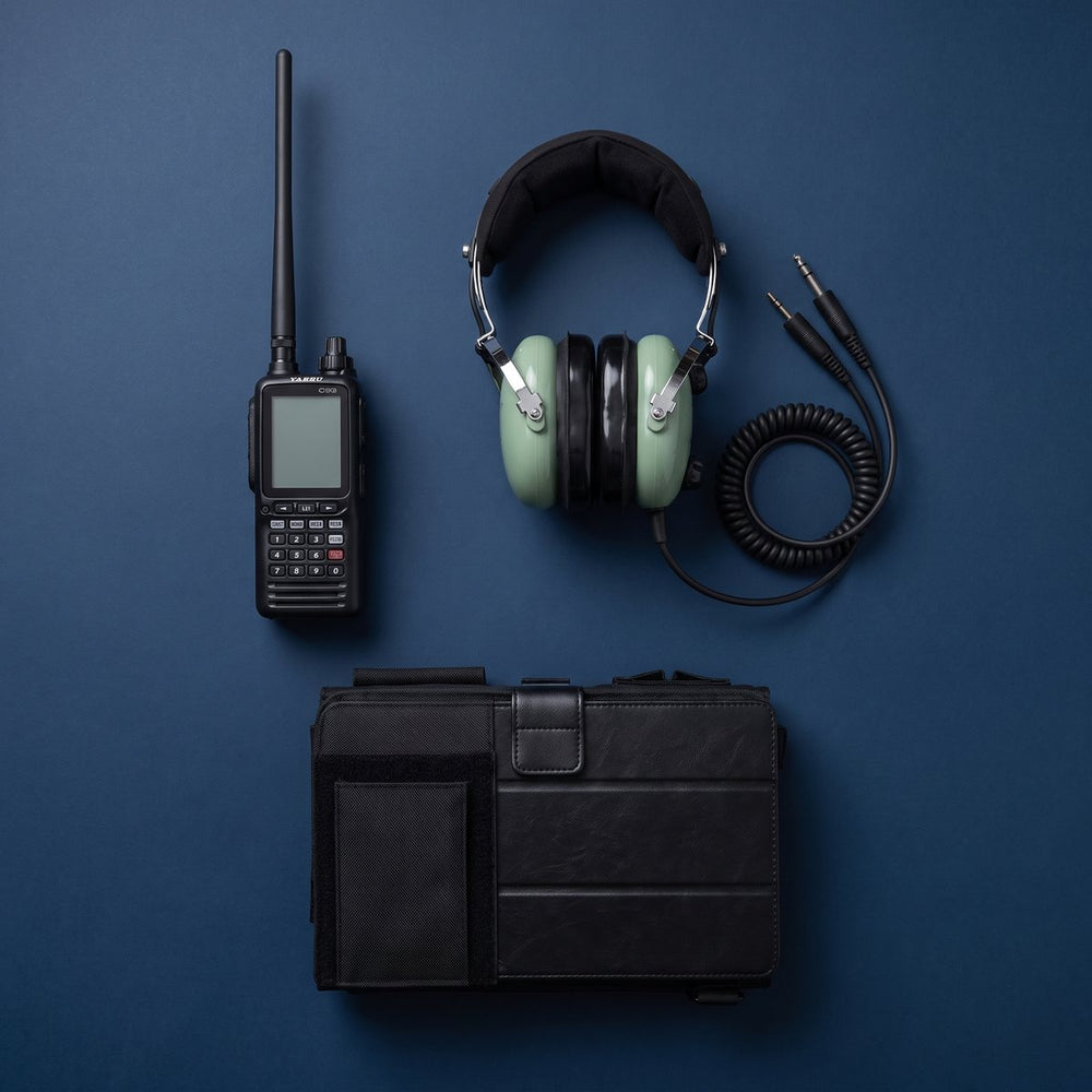 Radio Yaesu FTA-850L apagado junto a un headset David Clark de doble plug y una piernera sobre fondo azul marino
